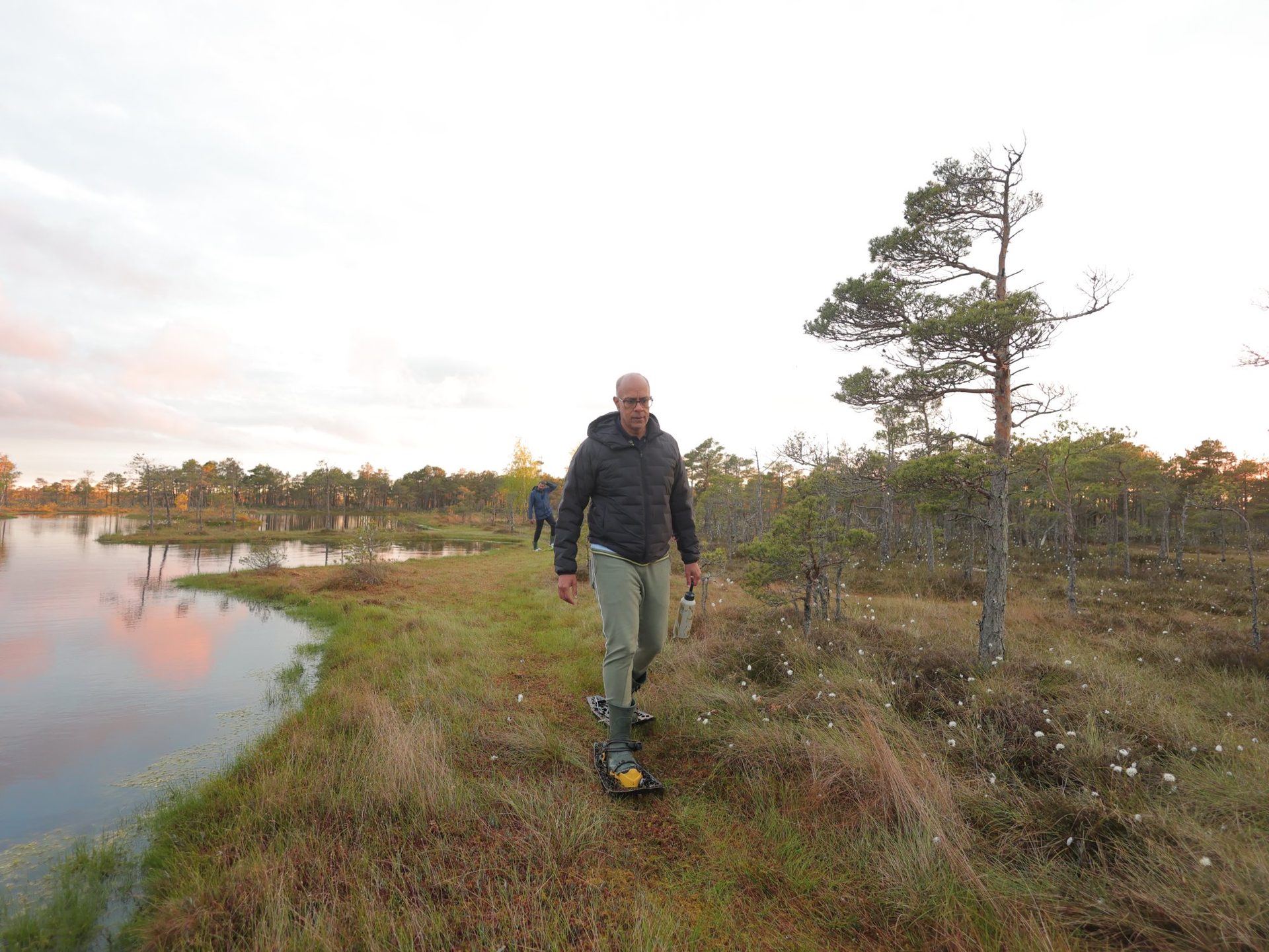 Solo walker in bog shoes beside a bog pool reflecting pink dawn light