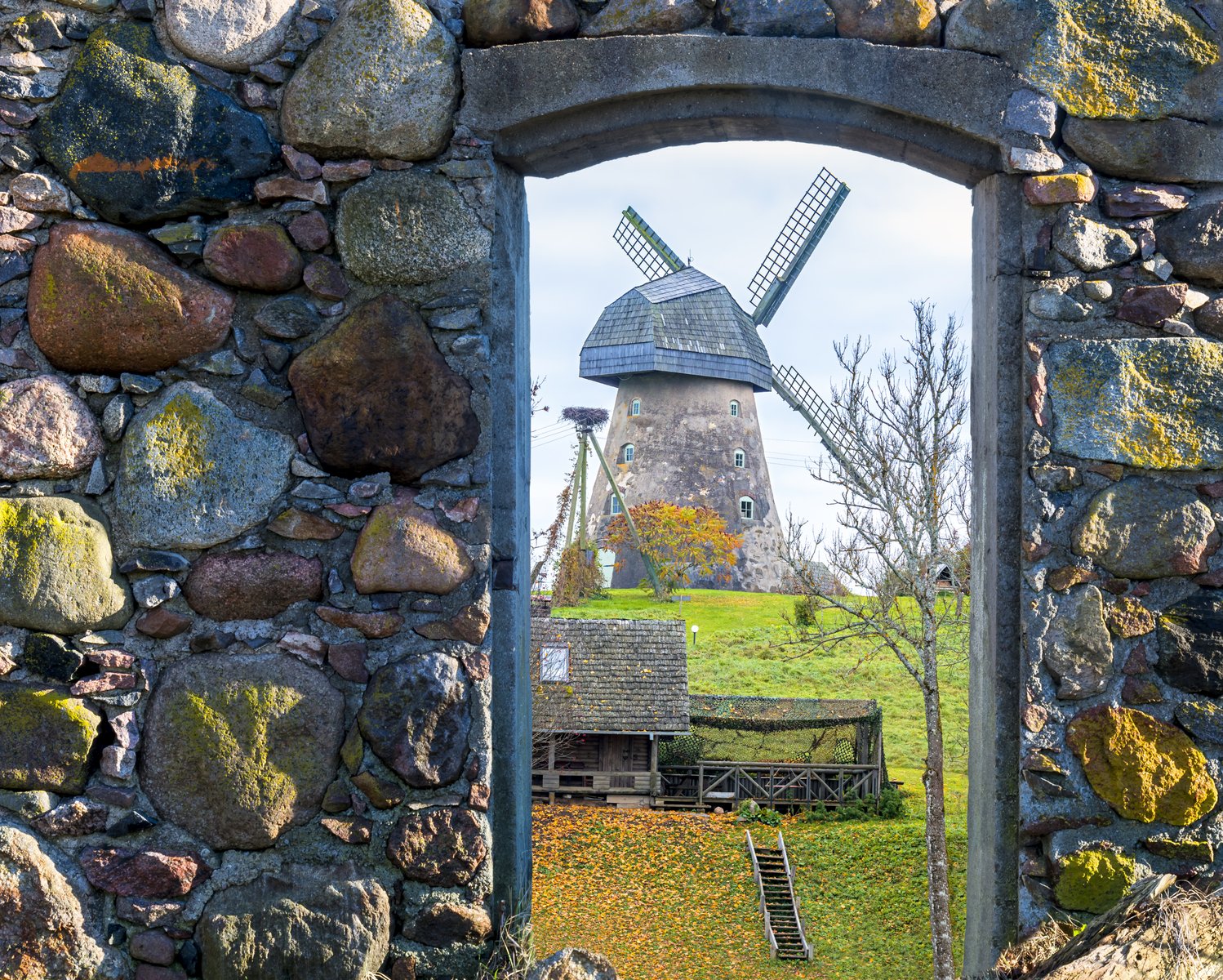 A traditional windmill seen through a stone archway on a Vidzeme farmstead