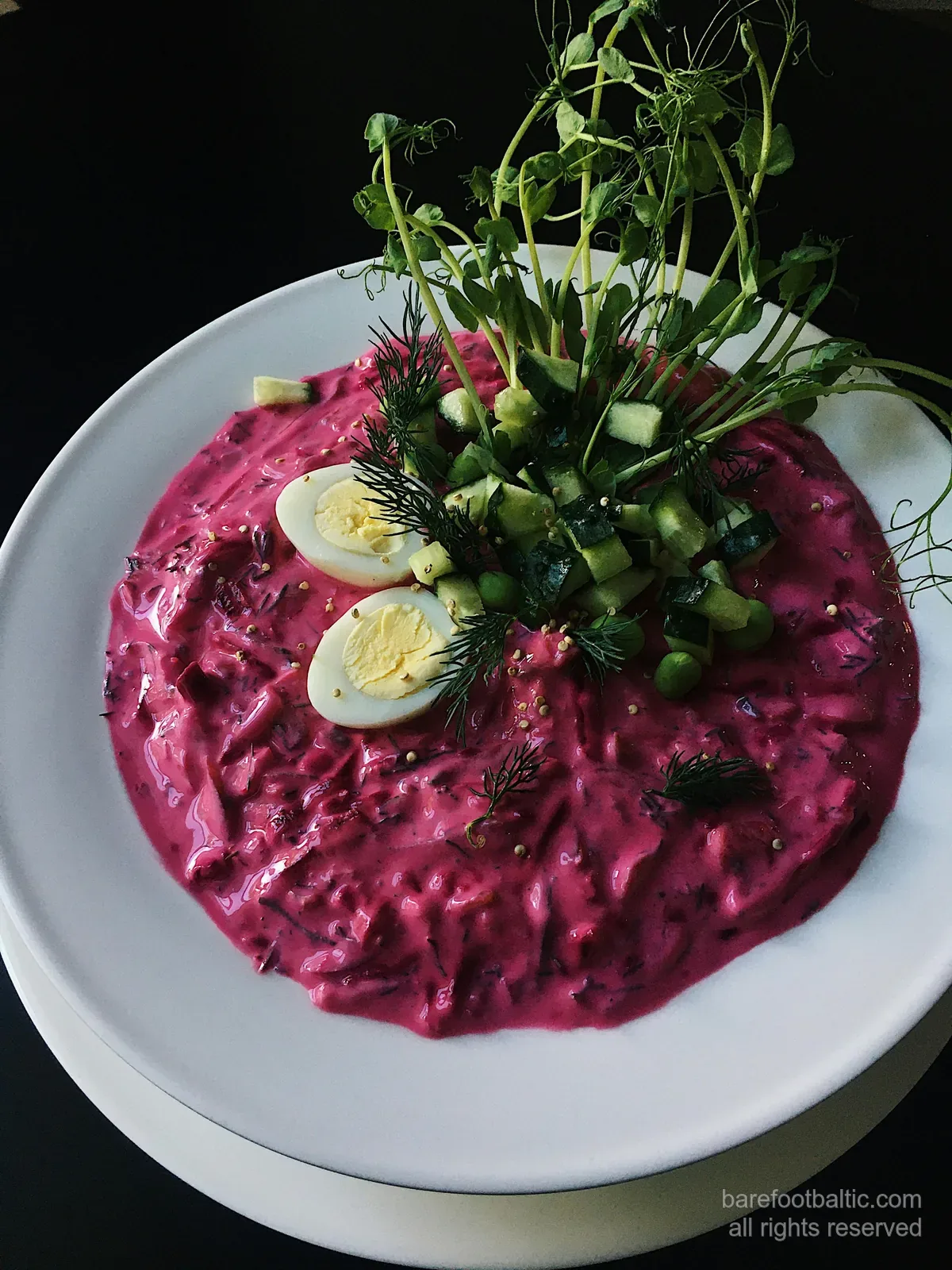 A bowl of bright pink aukstā zupa, the Latvian cold kefir-and-beetroot summer soup, garnished with hard-boiled egg, cucumber and dill