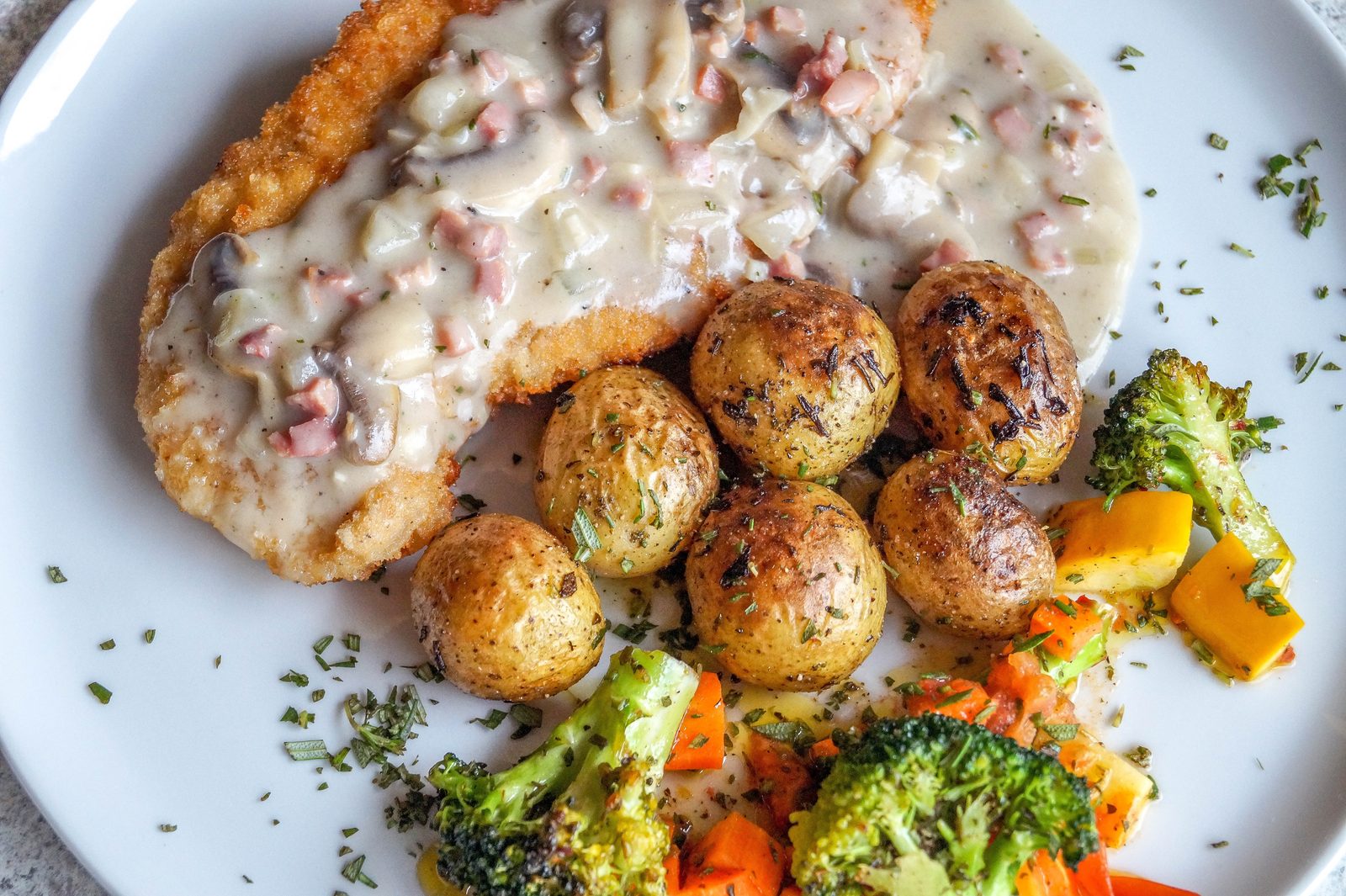 A plate of karbonāde — Latvian breaded pork cutlet — with creamy mushroom sauce, herbed potatoes and roasted vegetables