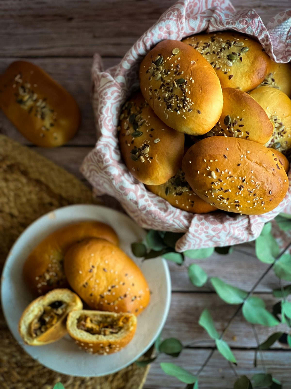 A basket of golden Latvian pīrāgi sprinkled with seeds, traditional small filled buns