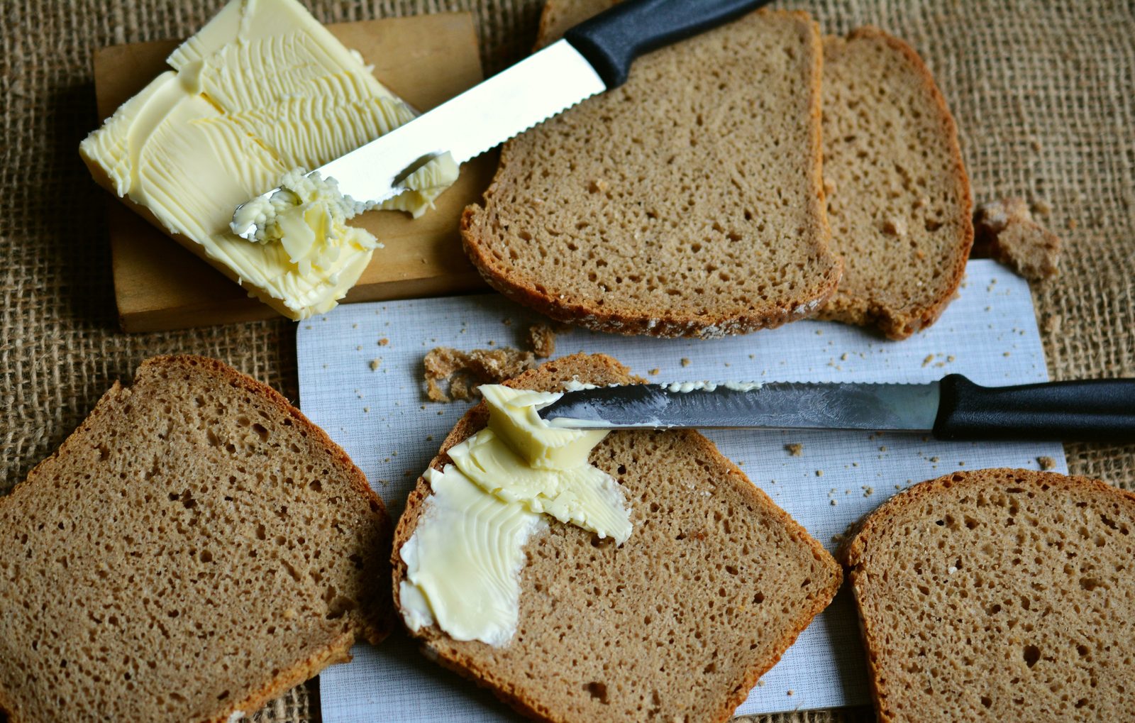 Slices of rupjmaize Latvian rye bread with butter and a knife on burlap