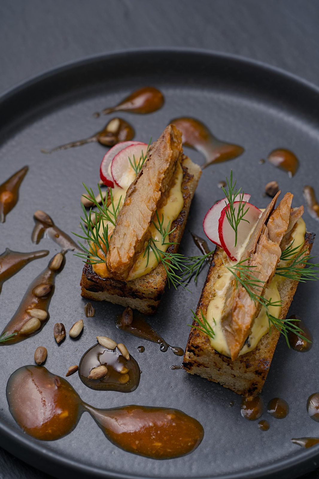 Smoked fish appetiser on toasted rye with cream, dill and radish, served on a black plate